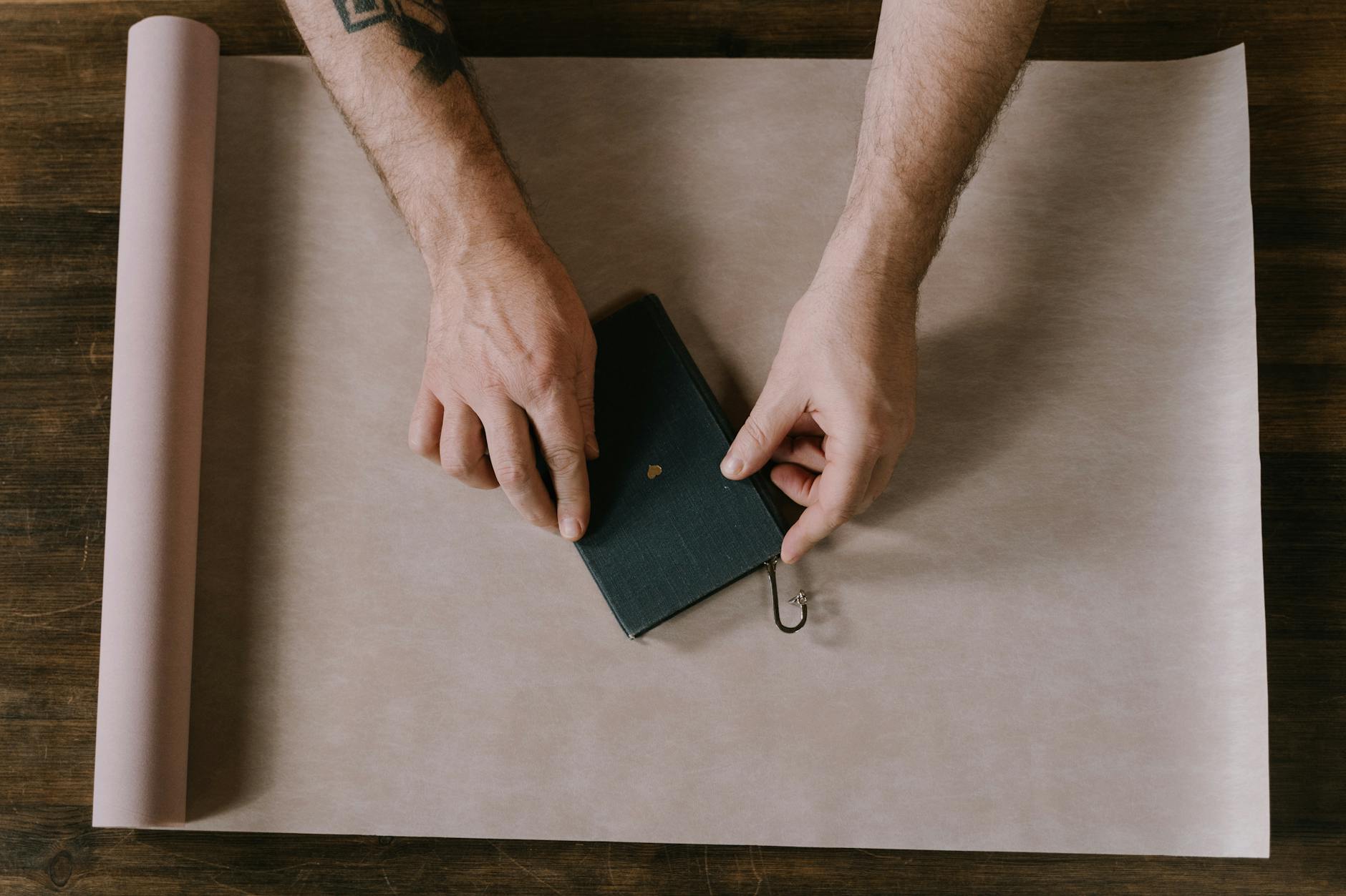 Dłonie pakujące książkę w brązowy papier na prezent