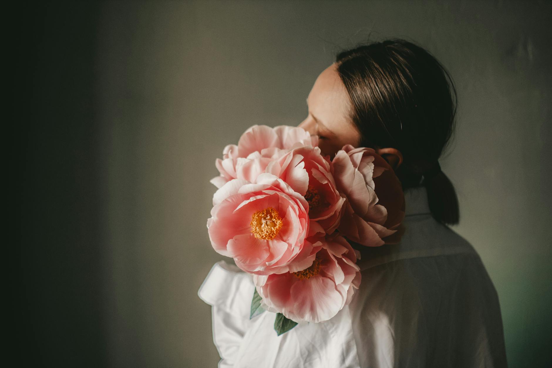 Kobieta trzyma bukiet różowych piwonii w romantycznym, domowym wnętrzu