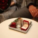 Prezenty premium dla miłośnika kawy: ekspres, młynek, akcesoria Pierścionek zaręczynowy w pudełku obok bukietu czerwonych róż na stole