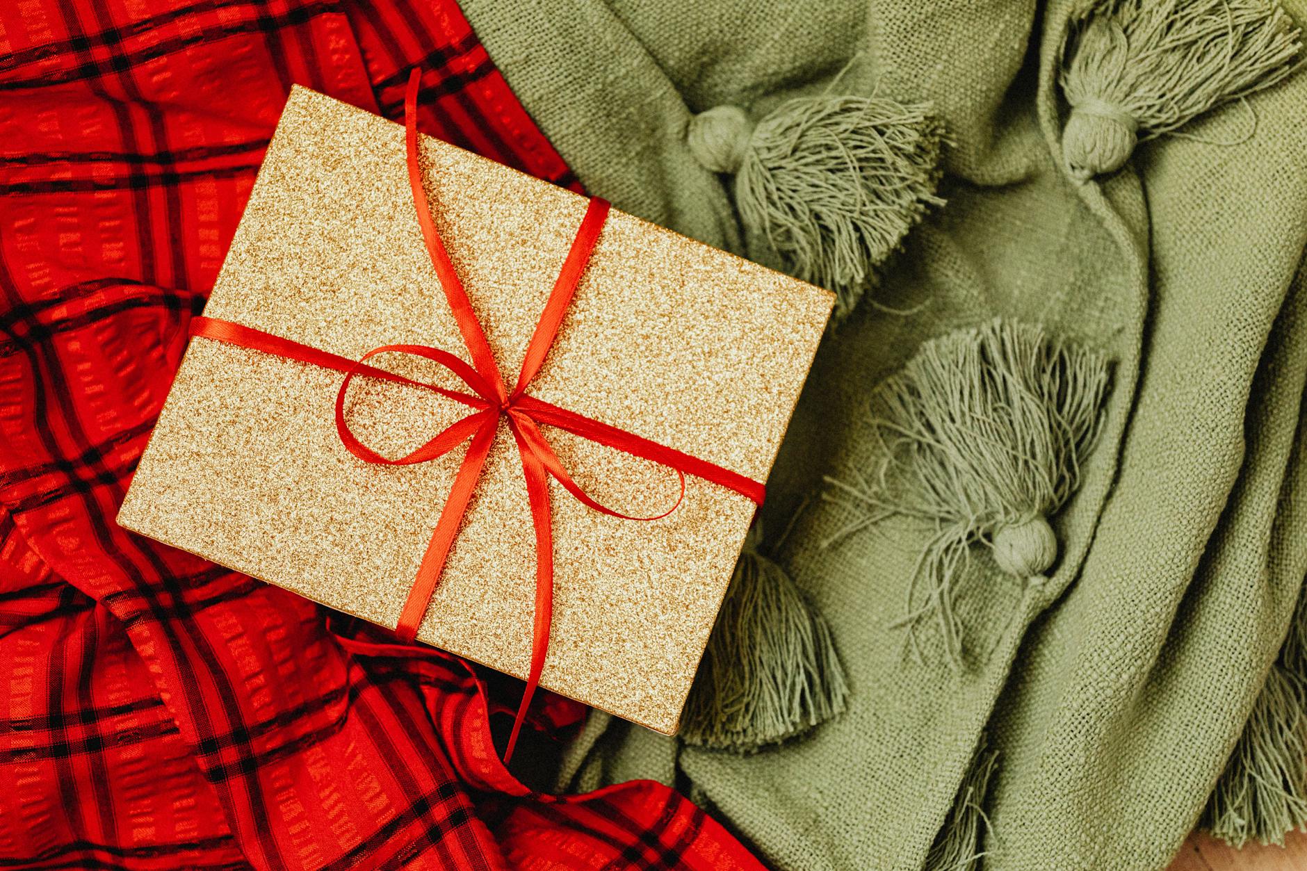 Złote pudełko prezentowe z czerwoną wstążką na miękkim kocu