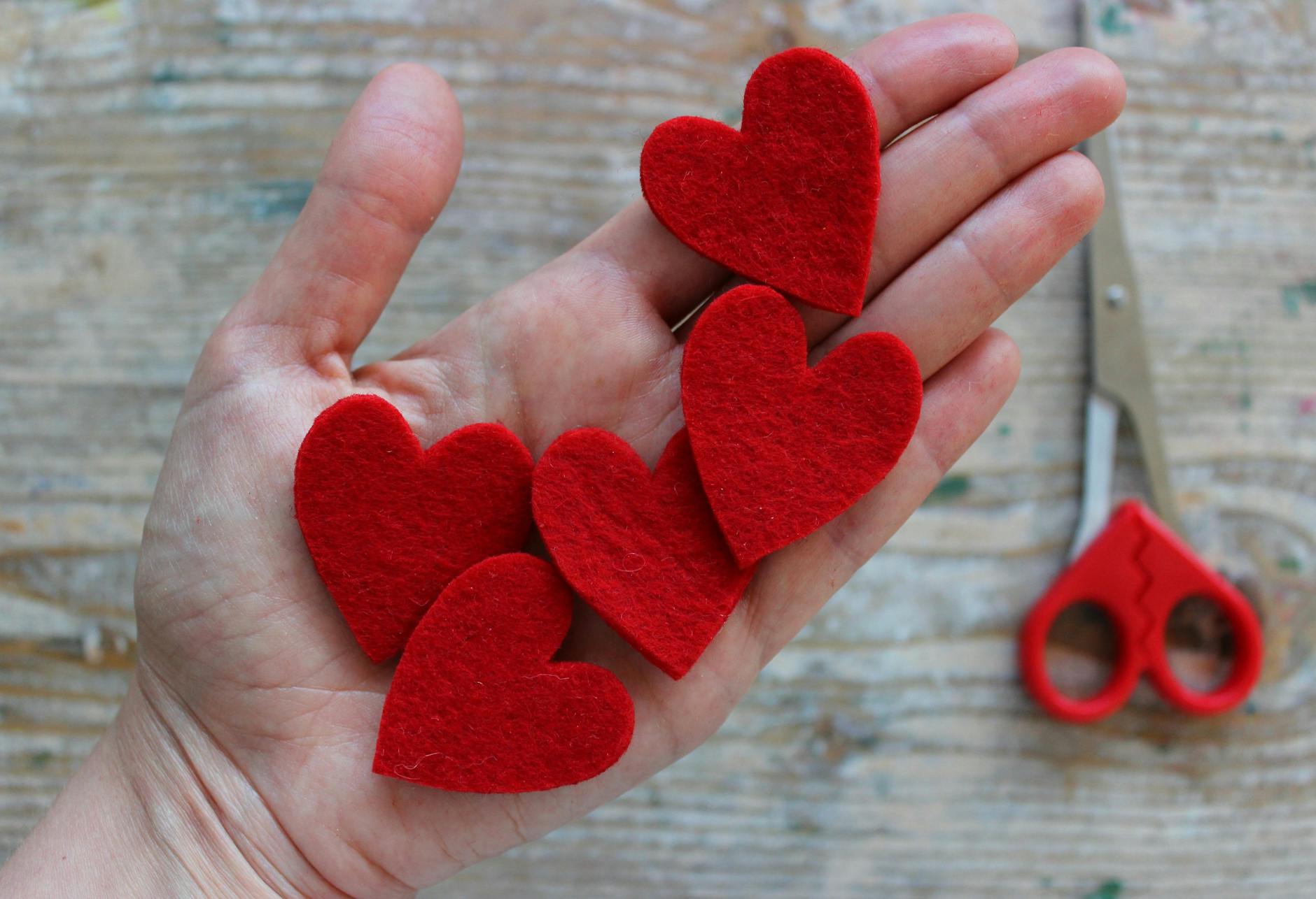 Dłoń trzymająca czerwone filcowe serduszka na drewnianym blacie