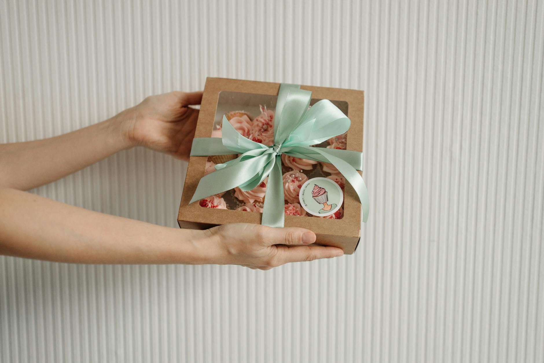 Dłonie trzymające ekologiczne pudełko prezentowe z babeczkami i miętową wstążką