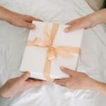 Symboliczny prezent na rocznicę, który mówi więcej niż kartka i kwiaty Dłonie wymieniające elegancko zapakowany prezent rocznicowy