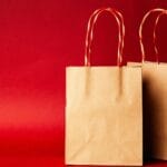 Co oznaczają certyfikaty FSC, GOTS i Fair Trade przy wyborze prezentu? Papierowe torby na prezenty na czerwonym świątecznym tle