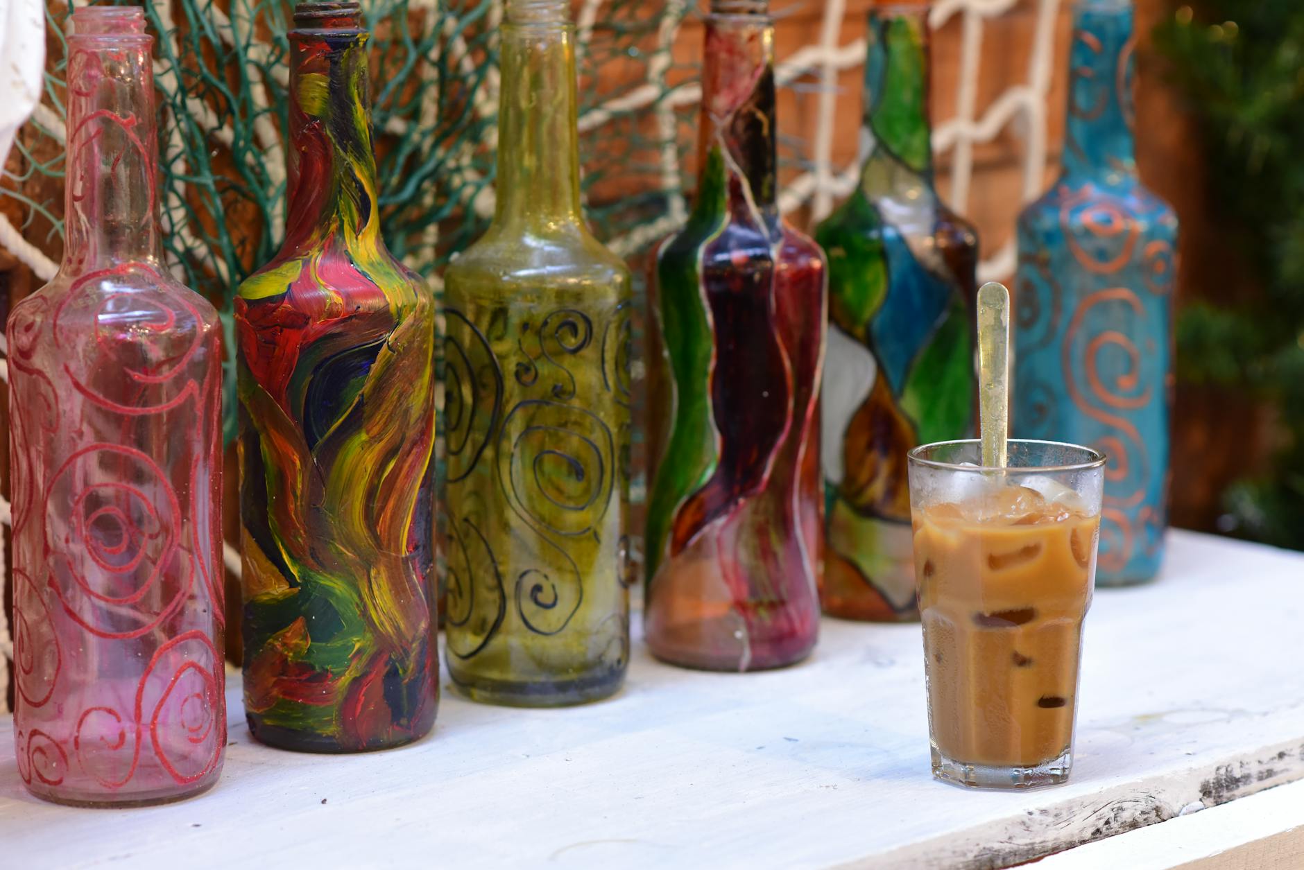 Ręcznie malowane butelki obok kawy mrożonej na rustykalnym stole na zewnątrz