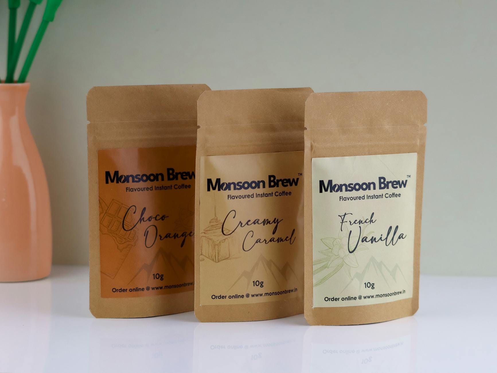 Trzy saszetki kawy Monsoon Brew na stole obok wazonu z kwiatami