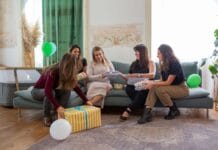 Prezent na baby shower od szefowej i zespołu z pracy – 8 eleganckich propozycji firmowych Kobiety świętujące baby shower i wręczające prezenty w domu