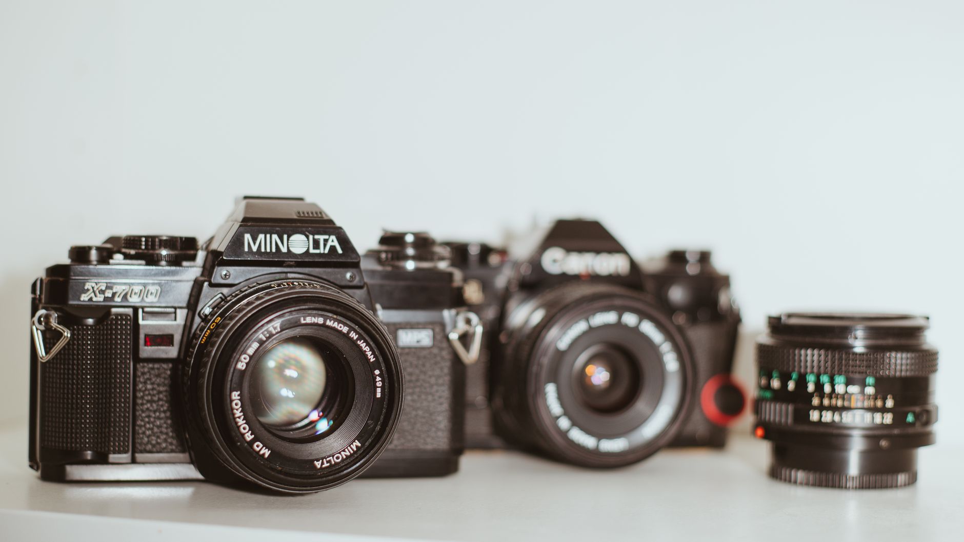 Aparaty analogowe Minolta i Canon z obiektywem na białym tle